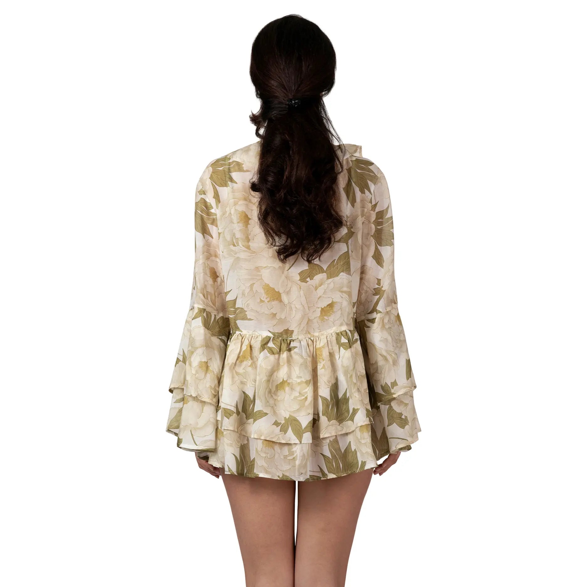 Woman wearing the FLEUR DE LUMIÈRE Short Tunic by BILEYA COUTURE, crafted from luxurious silk-cotton chiffon with a romantic white peony floral print, voluminous ruffle sleeves, and an airy designer resort wear silhouette.
