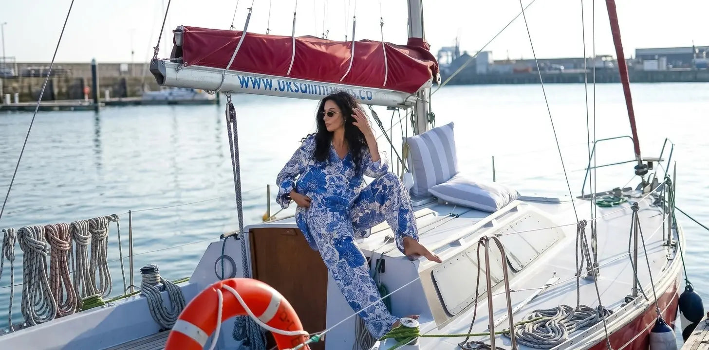 Woman in a blue floral outfit on a sailboat with water and cityscape in the background