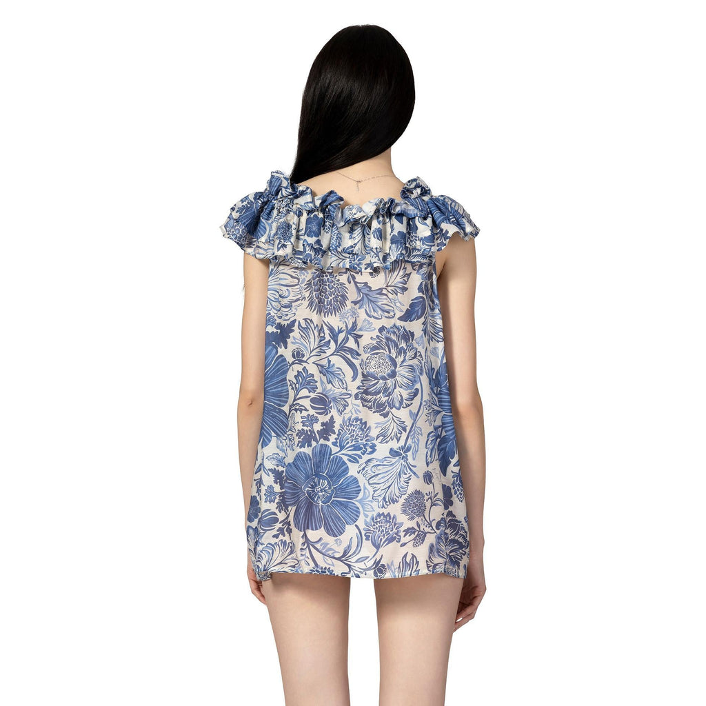 Woman wearing the MORGANA Sleeveless Resort Top by BILEYA COUTURE with blue floral print and elegant ruffle details